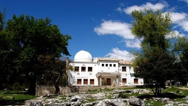 Edificio blanco del Centro de La Fresnedilla con su cúpula de observación, rodeado de árboles en la Sierra de las Villas